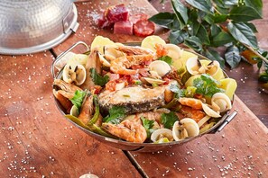 Un plat de fruits de mer composé de crevettes, de palourdes et de poisson, agrémenté d’herbes et de tranches de citron, servi sur une table en bois.