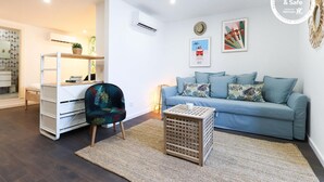 Un salon moderne avec un canapé bleu clair, un fauteuil à motifs, une petite table en bois et un bureau blanc agrémenté d’une plante.