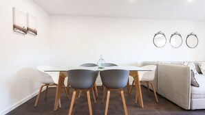 A modern dining area with a glass table, wooden chairs, and a white sofa. - Benfica Apartments III by Homing (Lisbon)