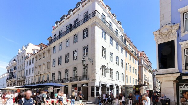 Un edificio histórico de varios pisos, con amplios ventanales y acceso por una esquina.