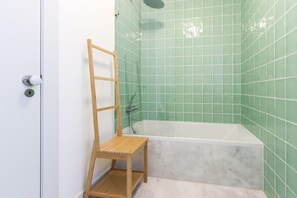 A bathroom with a bathtub, green tiled walls, and a wooden chair. - Downtown Santa Justa by Homing (Lisbon)
