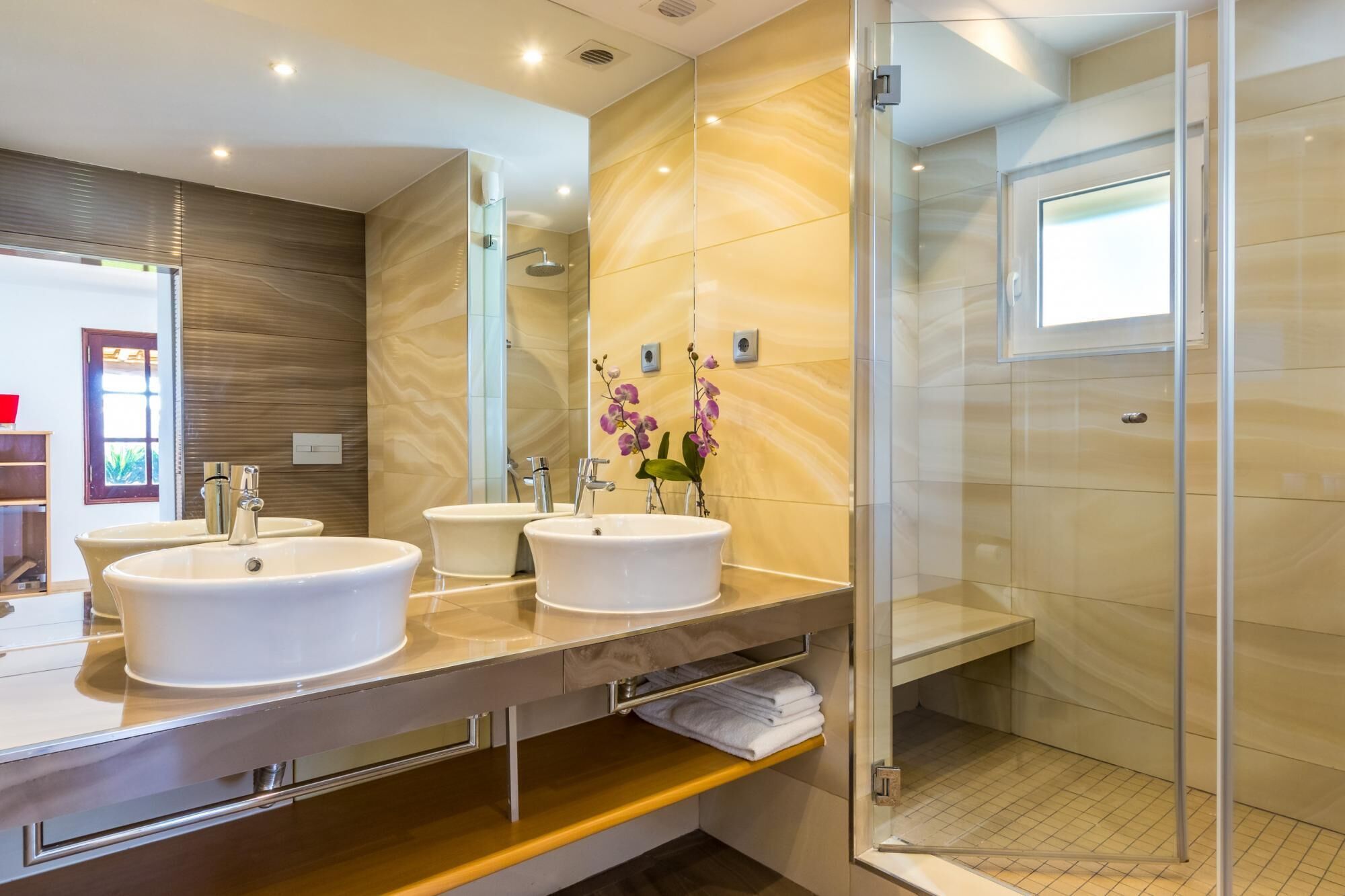 A modern bathroom with three sinks, a glass shower enclosure, and a wooden vanity.