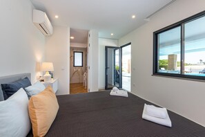 A modern hotel room with a large bed, a bedside table with a lamp, a view of the outside through a large window, and a door leading to a balcony. - Quintinha da Balaia in Albufeira (Albufeira)