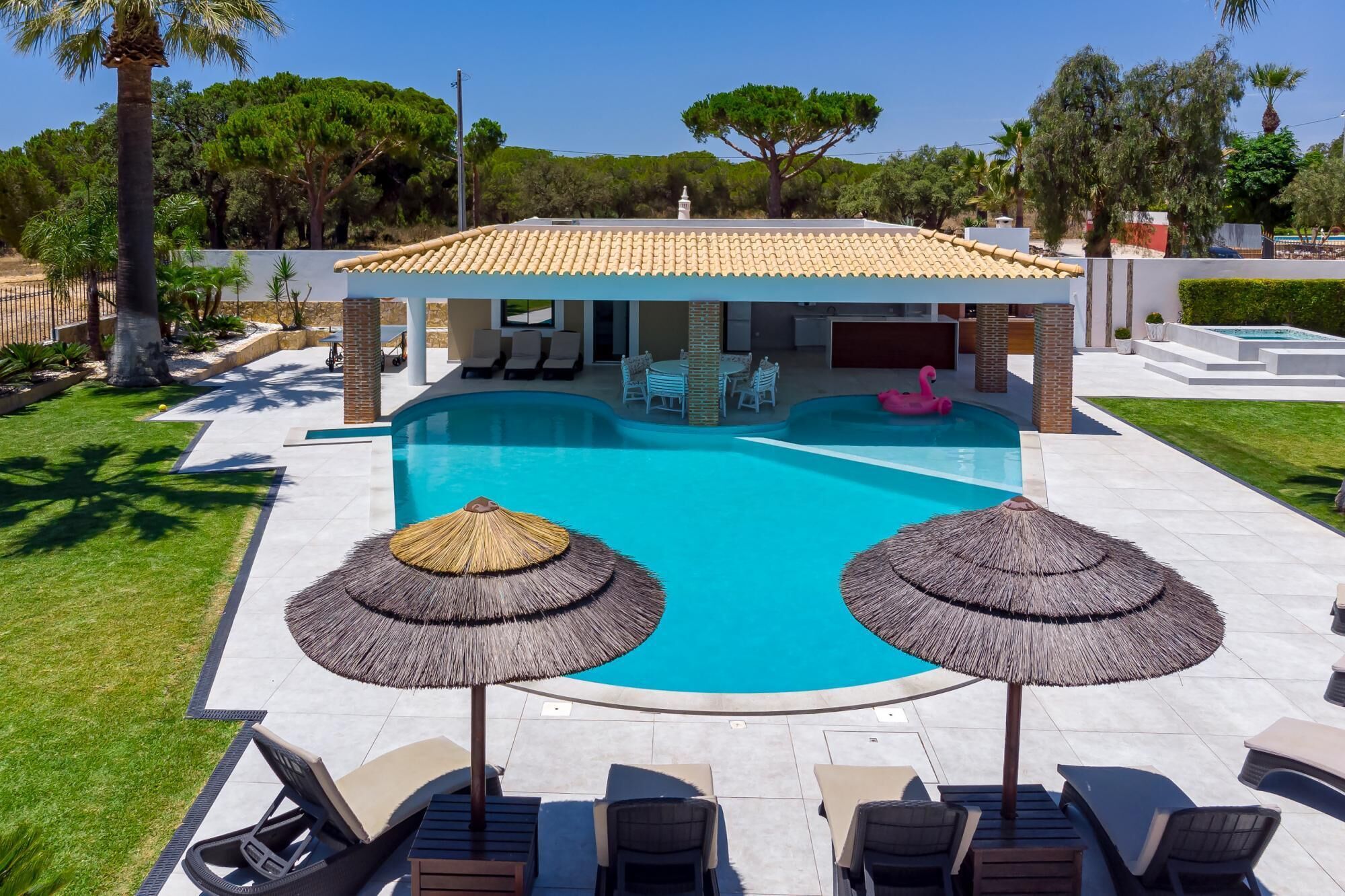 A swimming pool with lounge chairs and umbrellas, surrounded by a well-maintained lawn and trees.