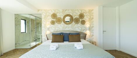A bedroom with a large bed, a glass shower enclosure, a wall-mounted mirror, and a patterned wall.