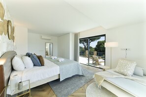 A modern bedroom with a bed, a sofa, a large window, and a view of the outdoors.