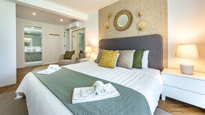 Une chambre d’hôtel avec un grand lit, une table de chevet avec une lampe, un miroir au mur et une vue sur la salle de bain.