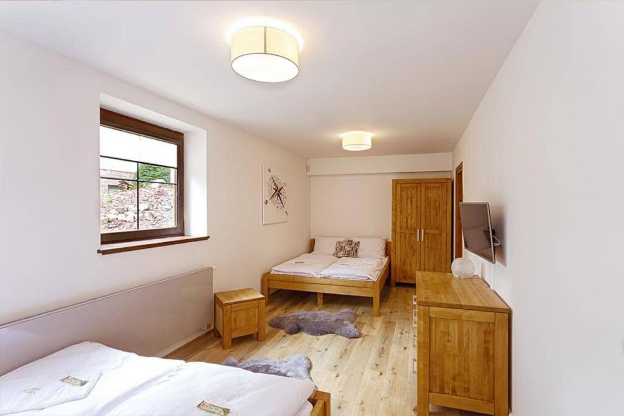 A bedroom with two beds, a wooden wardrobe, a television, and a window with a view of the outdoors.
