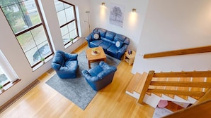 A spacious living area with a blue leather sofa, a wooden coffee table, and a grey rug. A wooden staircase is visible in the foreground. - Harrachov Lhje260 in Harrachov (Harrachov)