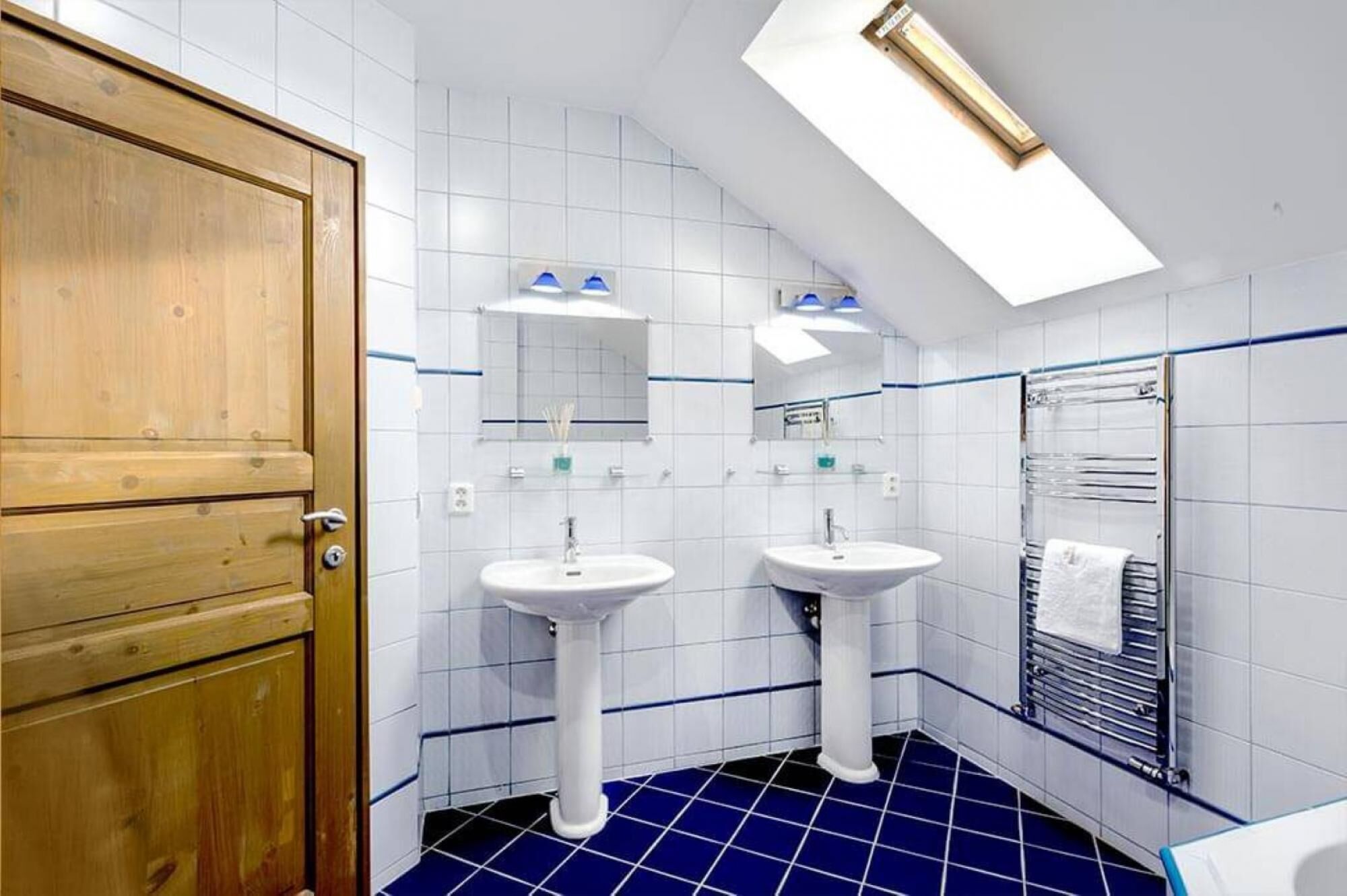 A bathroom with two sinks, a wooden door, and a skylight.
