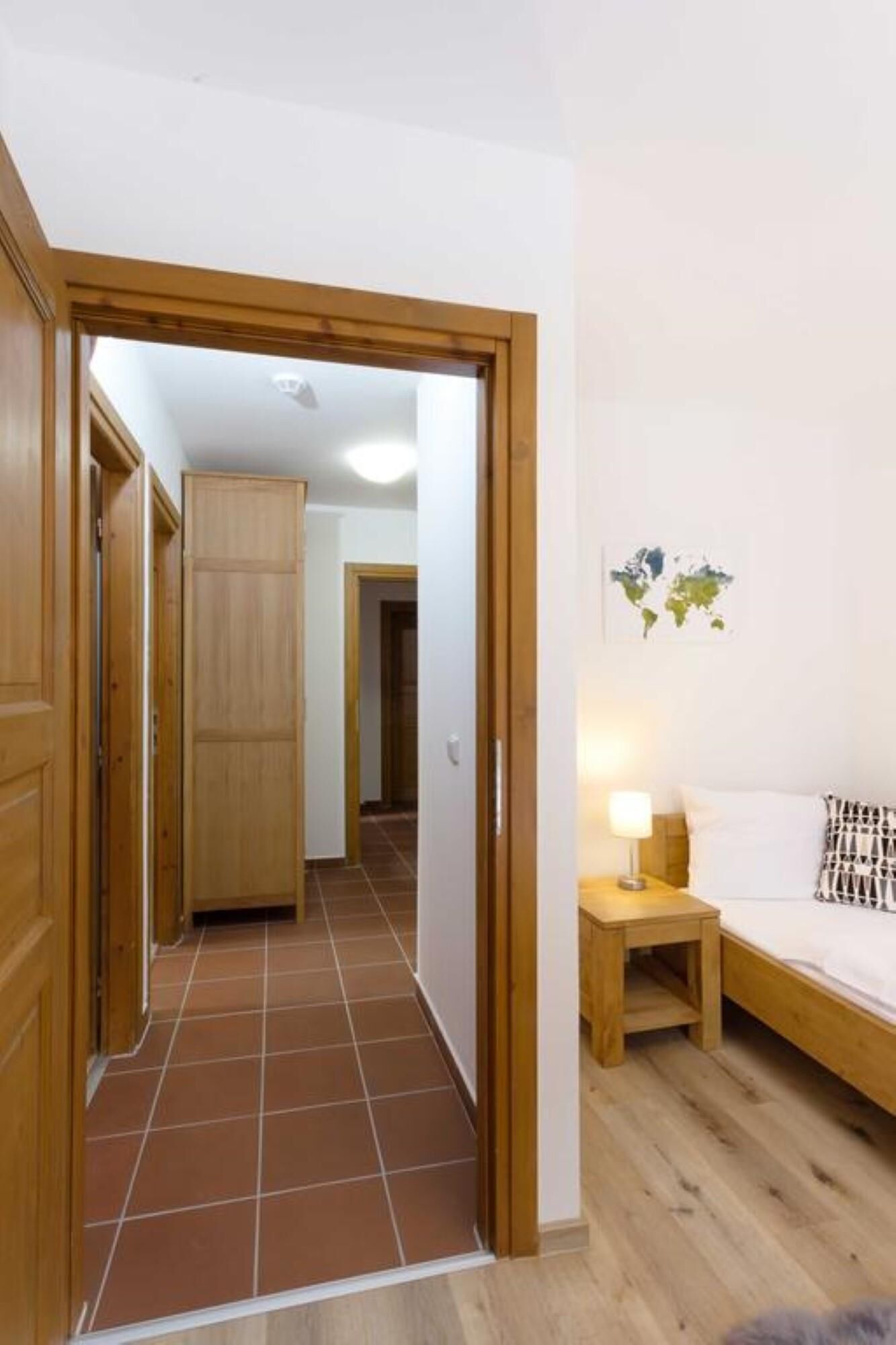 Un pasillo con puertas de madera que dan a una habitación con una cama, una mesita de noche y una lámpara de pared.