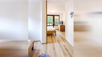 A room with a wooden floor, a bed, a dresser, and a television.