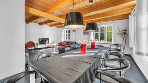 Une cuisine moderne avec un coin repas, des poutres apparentes en bois au plafond et de grandes fenêtres.