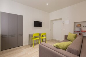 Un salon moderne avec un canapé gris, une petite table, deux fauteuils jaunes, un téléviseur à écran plat et une bibliothèque remplie de livres.
