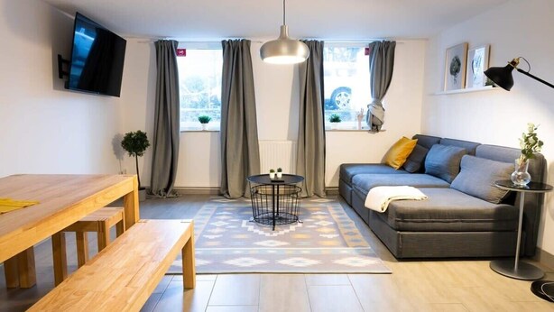 Una sala de estar moderna con una mesa de comedor de madera, un sofá gris, una mesa redonda de centro y un televisor montado en la pared.