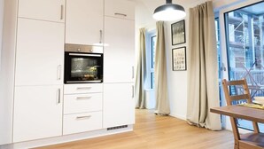 Een moderne keuken met witte kastjes, een ingebouwde oven en een eethoek met een houten tafel en stoelen.