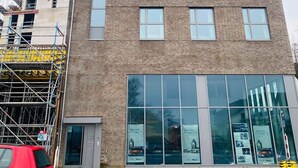 Een meerlaags gebouw met een moderne gevel van baksteen, grote ramen en een begane grond ingang met een glazen deur.