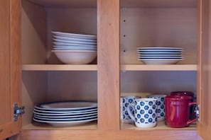 A wooden cabinet with shelves holding stacked plates and a few patterned mugs.