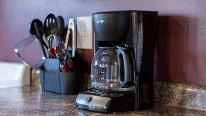 A coffee maker on a kitchen counter with a utensil holder in the background.