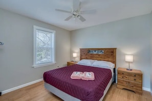A bedroom with a wooden headboard, a bed with a maroon bedspread, two bedside tables with lamps, and a ceiling fan.
