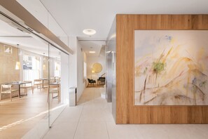 Un interior moderno con un mostrador de recepción de madera, un cuadro abstracto de gran tamaño y un separador de vidrio que divide un comedor del espacio principal.