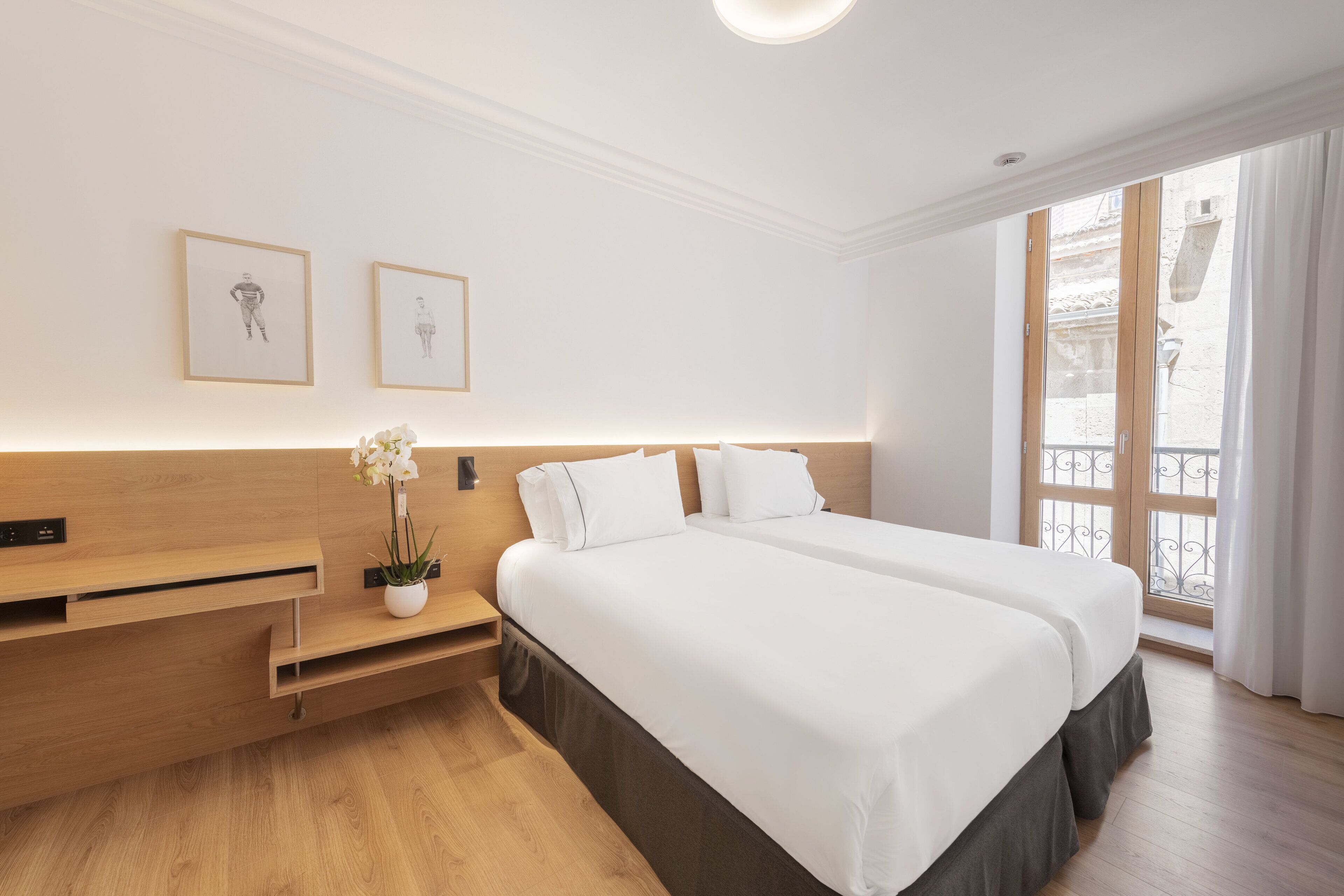 Une chambre d’hôtel avec deux lits, un bureau en bois, une petite plante et une fenêtre donnant sur l’extérieur.