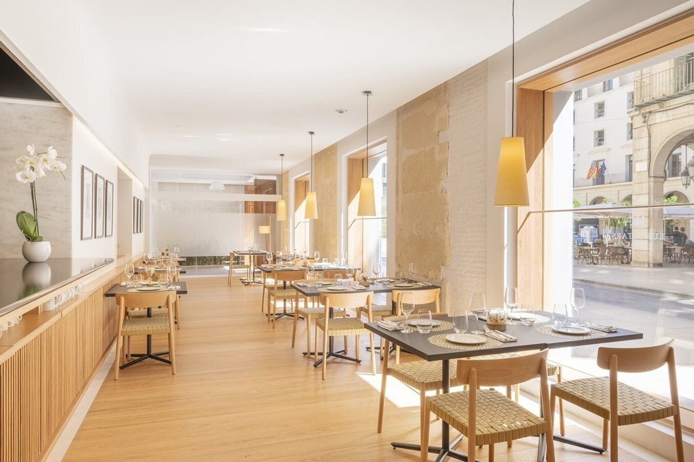 Un restaurant moderne avec des planchers et des tables en bois, de grandes fenêtres et des luminaires suspendus.