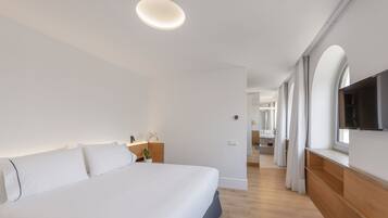Una habitación de hotel moderna con una cama grande, un televisor de pantalla plana montado en la pared y un banco de madera junto a la ventana.