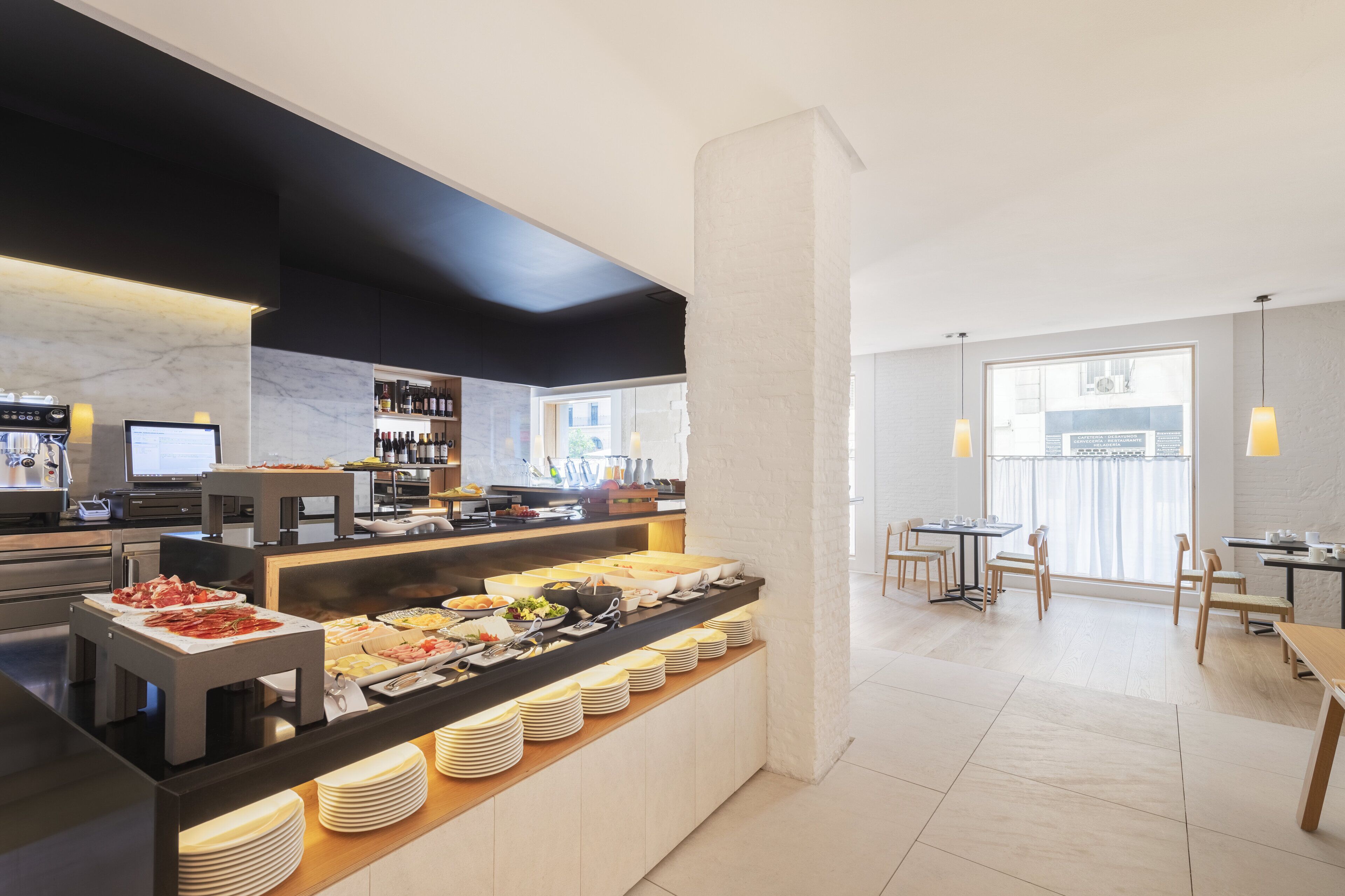 Een moderne hotelontbijtruimte met een buffet, een koffiehoek en zitplaatsen.