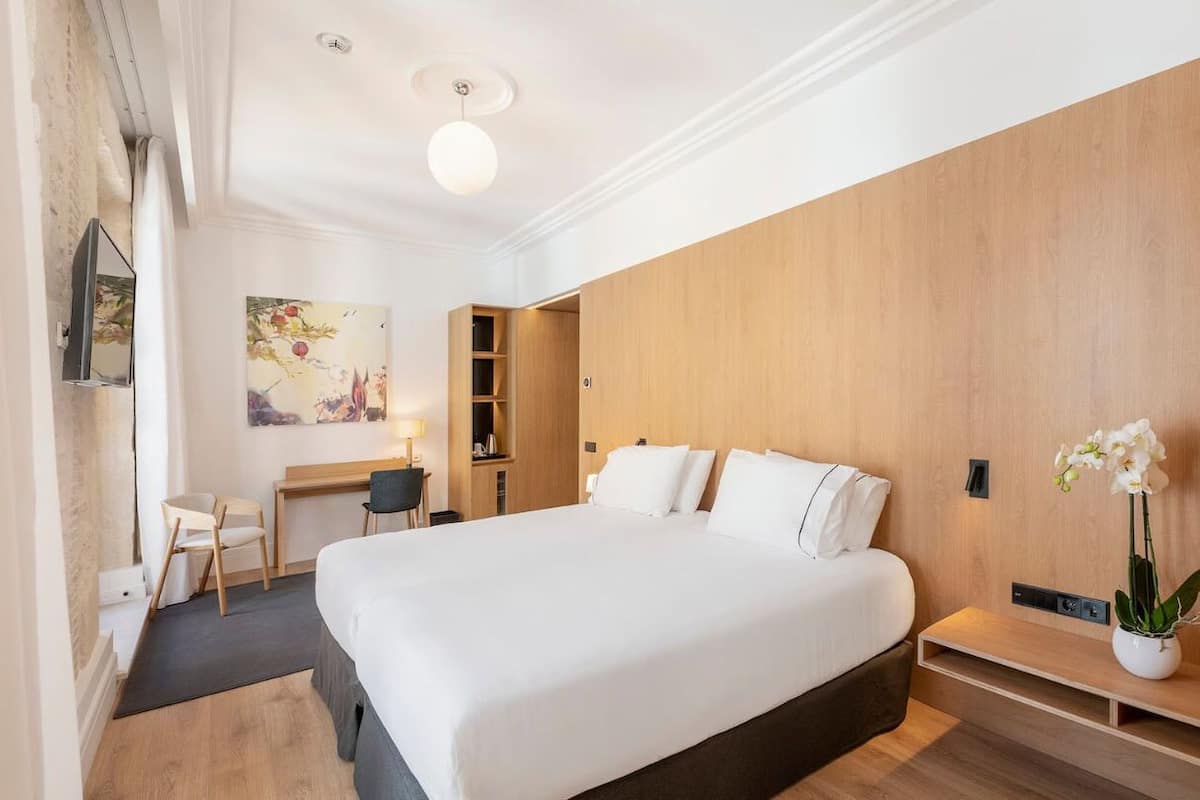 A modern hotel room with a large bed, a desk, and a chair.