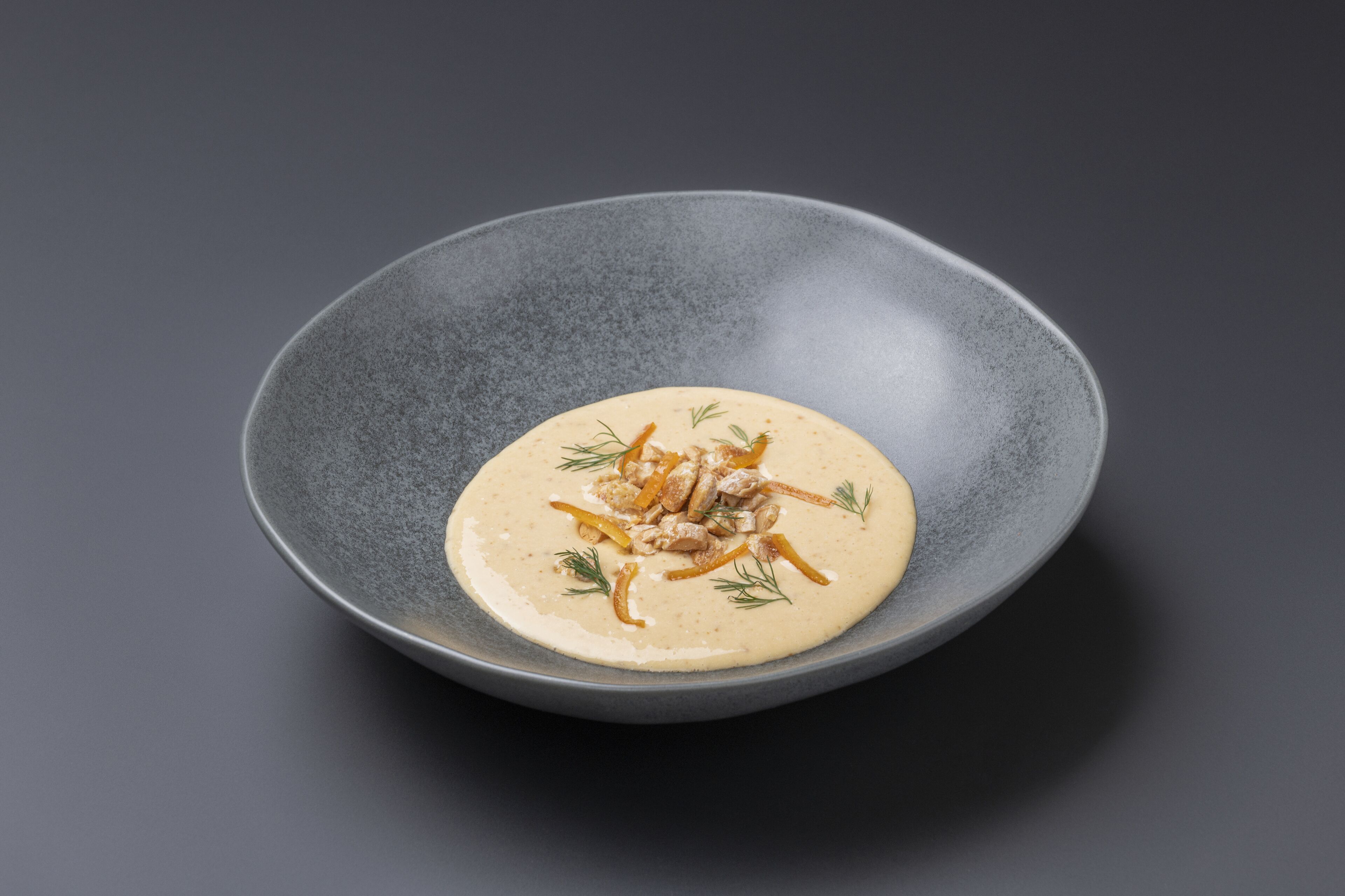 A dark gray plate with a creamy dish garnished with herbs and thin strips.