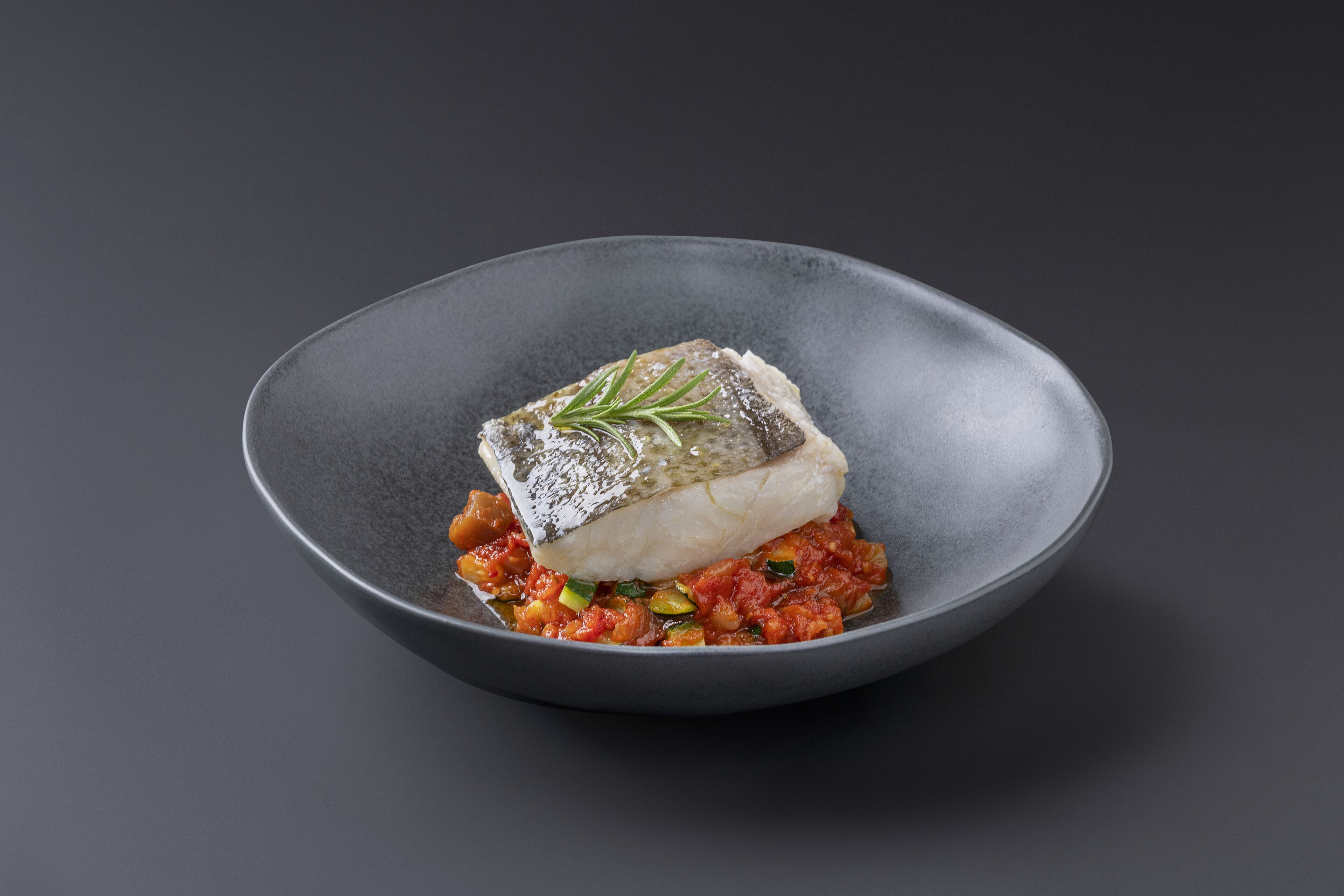 A dish of fish and vegetables on a dark plate.