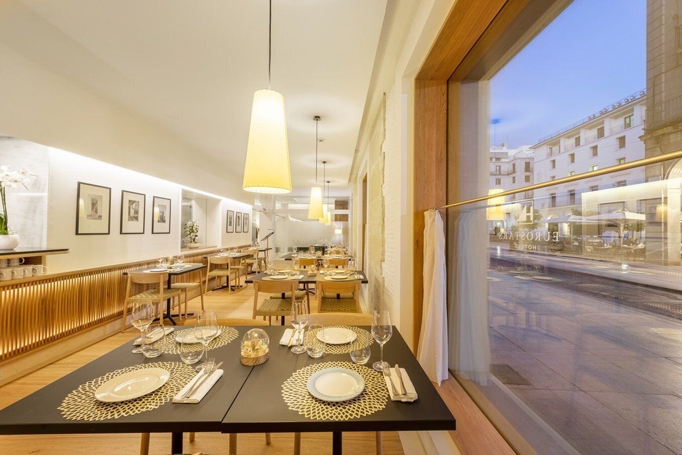 Ein Restaurant mit gedeckten Tischen, gerahmten Bildern an der Wand und Blick auf die Straße.