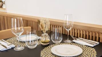 Mesa de jantar posta com taças de vinho, pratos e talheres, apresentando um centro de mesa decorativo e um sousplat texturizado.
