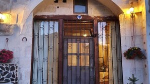 Ein Steinhaus mit rundbogenförmigem Eingang, einer Holztür mit Metallgitterstäben und zwei Wandleuchten.