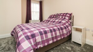 A bedroom with a bed, a nightstand, a window with curtains, and a carpeted floor. - 1 Tregonwell Court (Minehead)