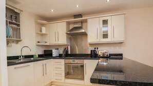 A modern kitchen with white cabinets, a black countertop, and a stainless steel range hood. - 1 Tregonwell Court (Minehead)