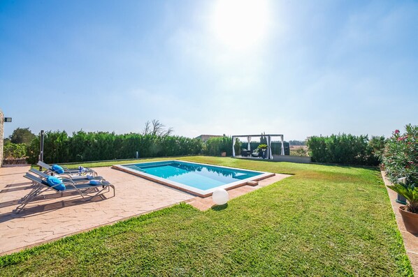 A rectangular swimming pool with a clear blue water surface, surrounded by a well-maintained lawn and a brick patio area with lounge chairs.