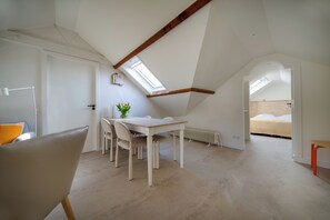 Una habitación con techo inclinado, una mesa de comedor con sillas, una cama y un radiador.
