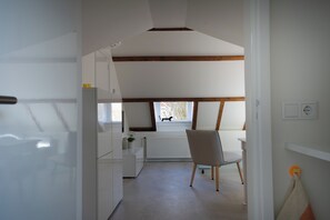 Un pasillo estrecho que conduce a una cocina con ventana, un radiador y una silla.
