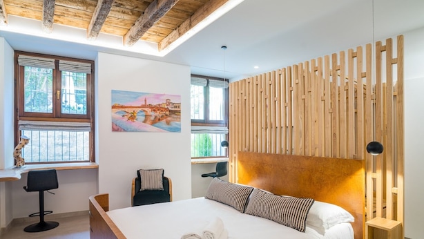 A modern bedroom with a wooden headboard, a bed with white linens, a desk with a chair, and a painting on the wall. - Design Rooms Verona (Verona)