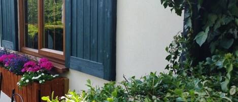 Una ventana con contraventanas azules, un banco de madera y una maceta con flores.