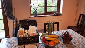 Uma área de refeições com mesa posta para o café da manhã, com uma cesta de frutas, uma garrafa de suco e uma cesta de doces.