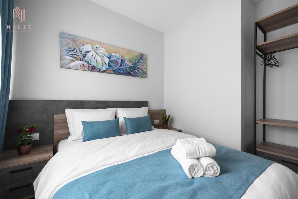 Una habitación de hotel moderna con una cama bien hecha, una manta azul y un cuadro sobre la cama.