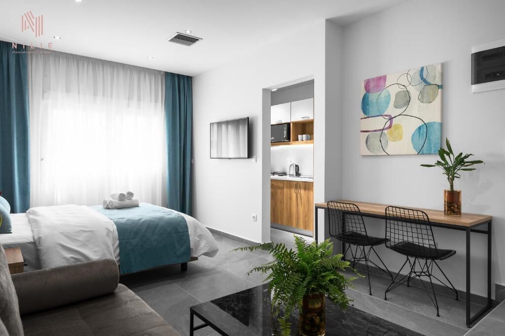 Ein modernes Hotelzimmer mit einem Bett, einem Schreibtisch mit zwei Stühlen, einer kleinen Küchenzeile und einem großen, abstrakten Gemälde an der Wand.