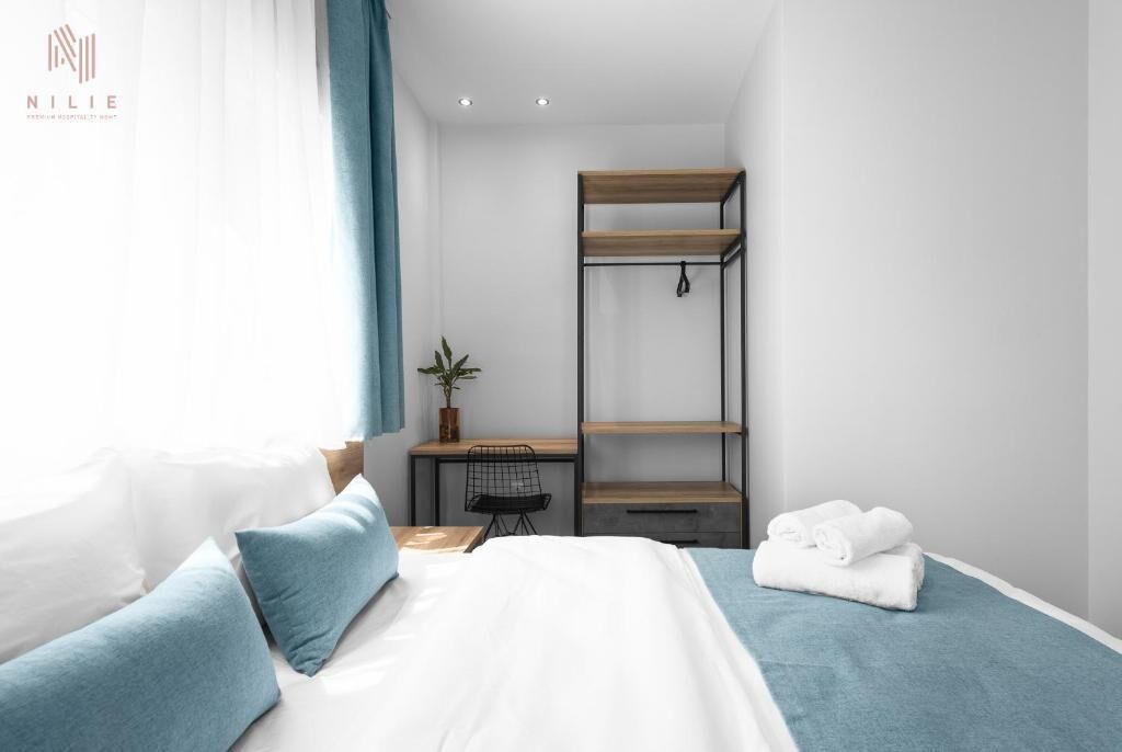 A modern hotel room with a bed, a desk, and a shelving unit.