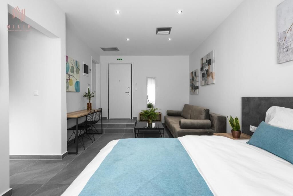 Moderni hotellihuone, jossa on sänky, sohva, ruokailutila ja pieni pöytä, jonka päällä on kasvi.