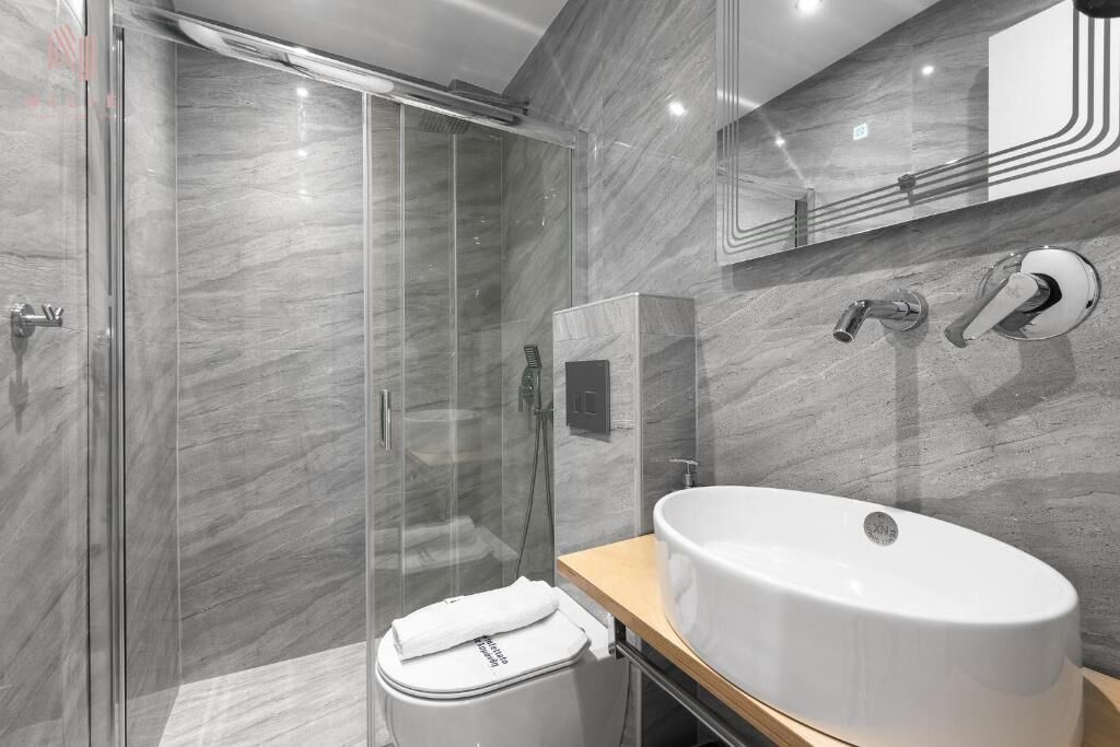 Ein modernes Badezimmer mit einer gläsernen Duschkabine, einem großen weißen Waschbecken und einer Marmorwand.