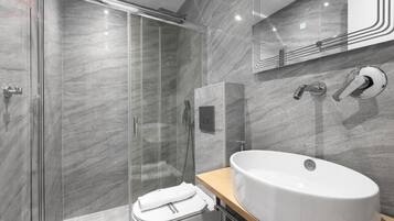 Ein modernes Badezimmer mit einer gläsernen Duschkabine, einem großen weißen Waschbecken und einer Marmorwand.