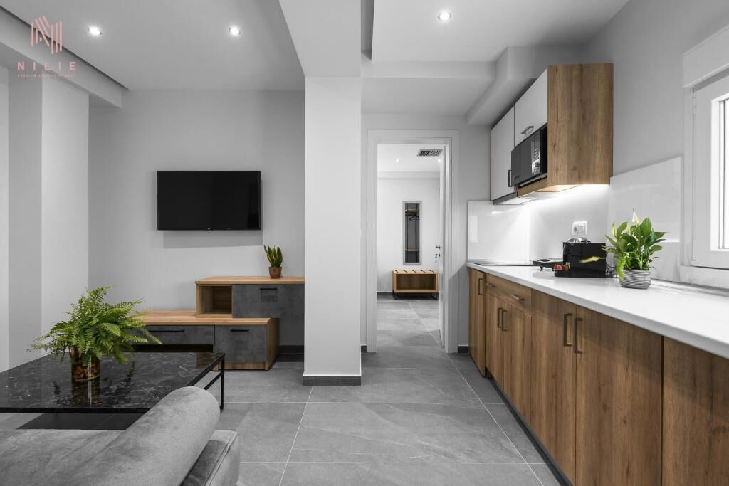 A modern kitchen with wooden cabinets, a black countertop, and a TV mounted on the wall.